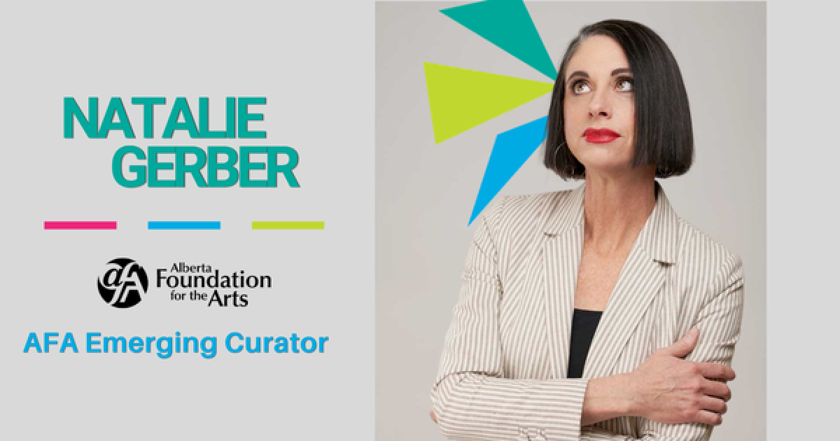 Natalie Gerber is photographed against a grey background with her arms crossed. She has brown hair, red lipstick, and is wearing a white and beige striped blazer and a black shirt underneath. 