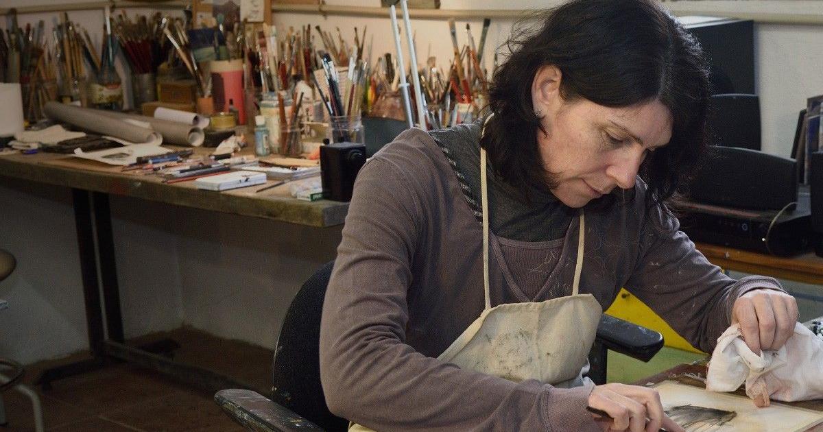 A woman sits in an art studio and draws on a piece of paper on a table