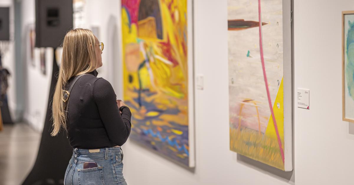 A guest is seen admiring an artwork while wearing blue jeans and a black blouse.