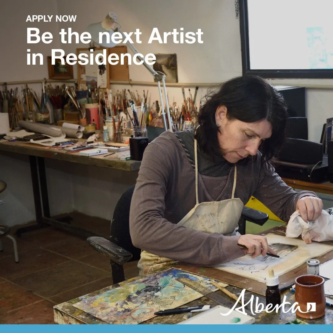 A woman sits in an art studio and draws on a piece of paper on a table