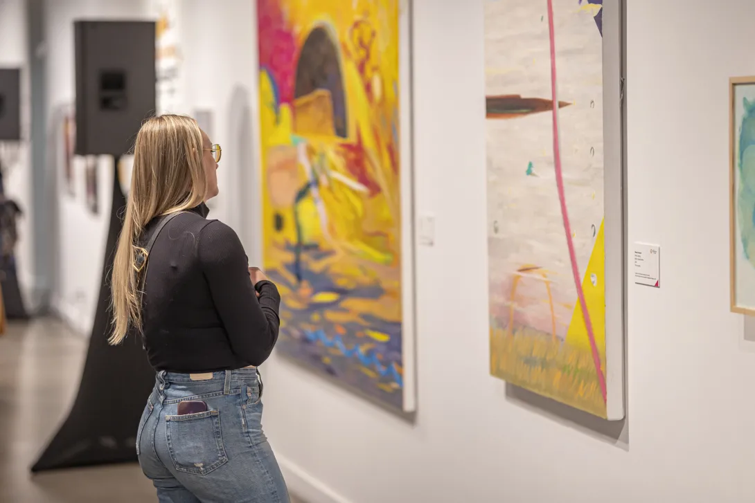 A guest is seen admiring an artwork while wearing blue jeans and a black blouse.